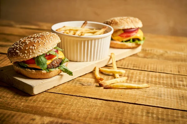 Dos sabrosas hamburguesas y papas fritas sobre tabla de madera y fondo negro — Foto de Stock