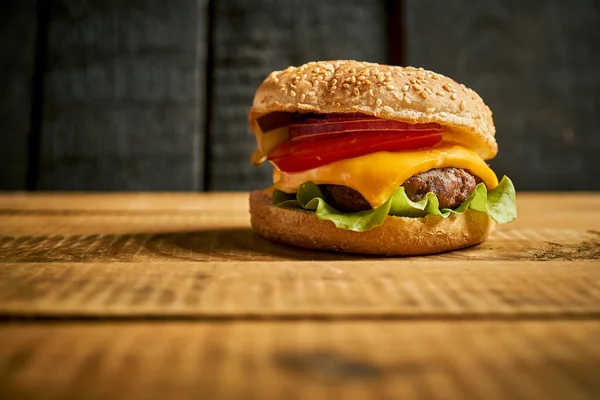 Primer plano de sabrosa hamburguesa sobre mesa de madera y fondo negro — Foto de Stock