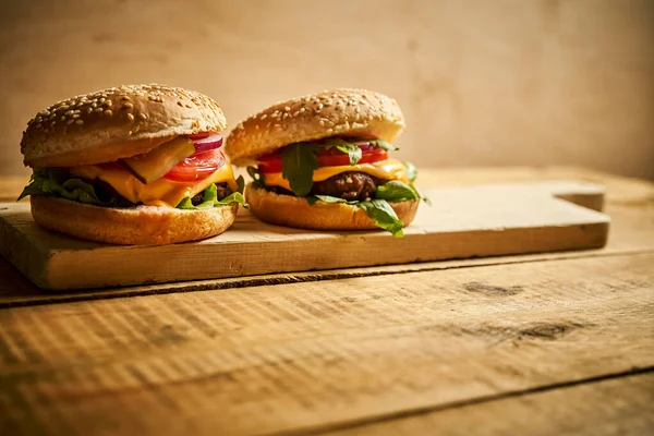 Dos sabrosas hamburguesas sobre tabla de madera y fondo negro — Foto de Stock