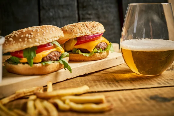 Dos sabrosas hamburguesas y papas fritas sobre tabla de madera y fondo negro —  Fotos de Stock