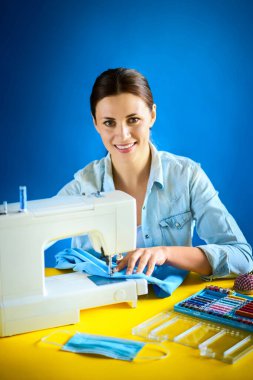 Karantina sırasında kadın makineye maske dikiyor.