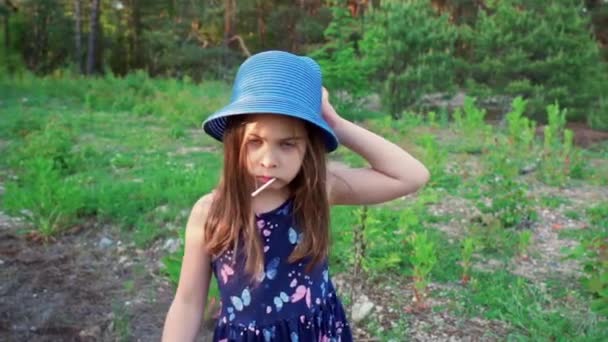 Liten flicka i en sommarklänning håller en trä leksak pistol i en tallskog — Stockvideo