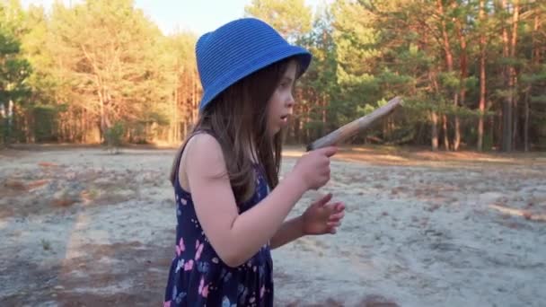 Klein meisje in een zomer jurk is met een houten speelgoed pistool in een dennenbos — Stockvideo