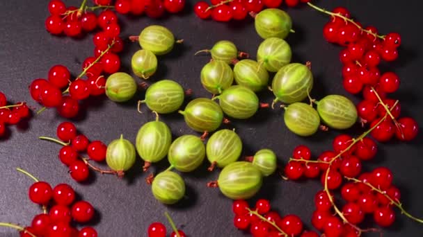 Pyszne czerwone żurawiny i soczyste zielone agrest na czarnym kamiennym stole — Wideo stockowe