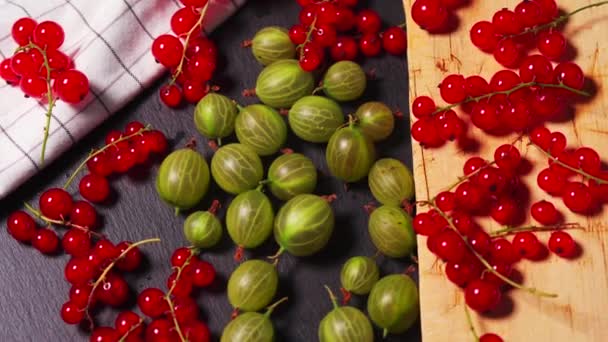 Köstliche rote Preiselbeere und saftige grüne Stachelbeere auf einem schwarzen Steintisch — Stockvideo