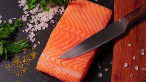 Köstlicher frischer Lachs mit Salz und Gewürzen auf einem Tisch aus schwarzem Stein — Stockvideo