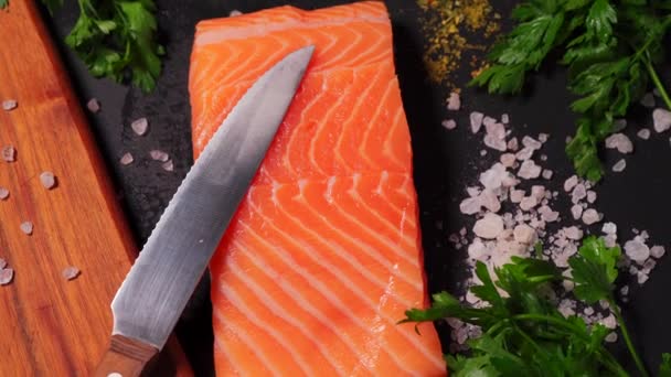 Вкусный свежий лосось с солью и специями на черном каменном столе — стоковое видео