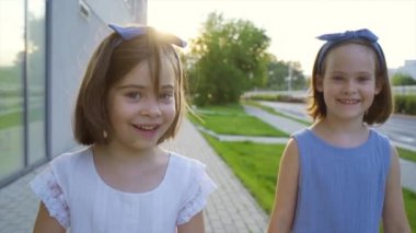 Gün batımında iki küçük tatlı kız şehir sokaklarında yürüyor.