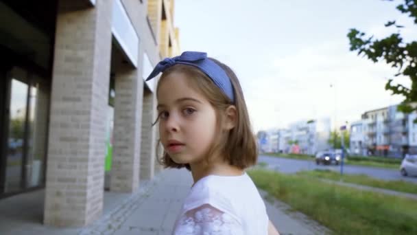 Söt liten flicka promenader längs stadens gator vid solnedgången — Stockvideo
