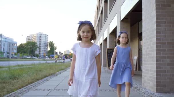 Két aranyos kislány sétál a város utcáin naplementekor. — Stock videók