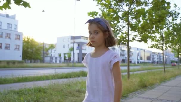 Aranyos kislány sétál a város utcáin naplementekor — Stock videók