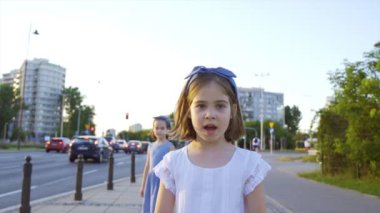 Gün batımında iki küçük tatlı kız şehir sokaklarında yürüyor.