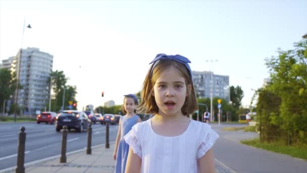 日落时分，两个可爱的小女孩沿着城市的街道走着 — 图库视频影像