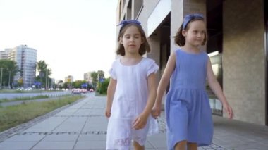 Gün batımında iki küçük tatlı kız şehir sokaklarında yürüyor.