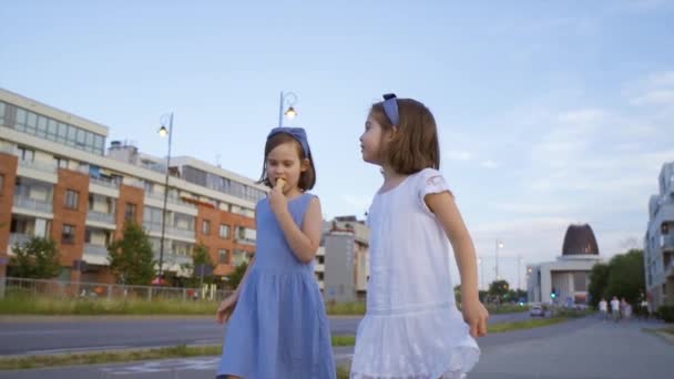 İki küçük tatlı kız şehirde dolaşıp dondurma yiyorlar. — Stok video