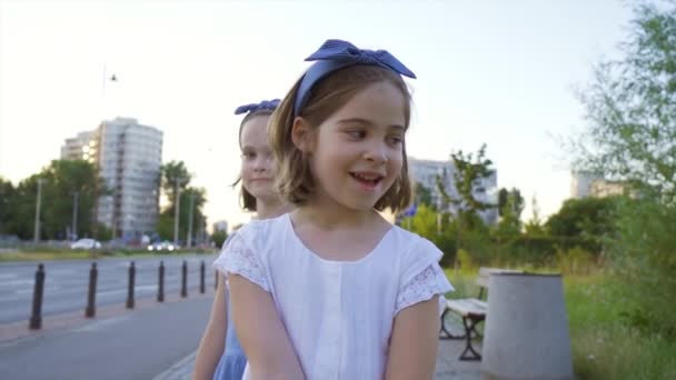 Deux jolies petites filles marchent le long des rues de la ville au coucher du soleil — Video