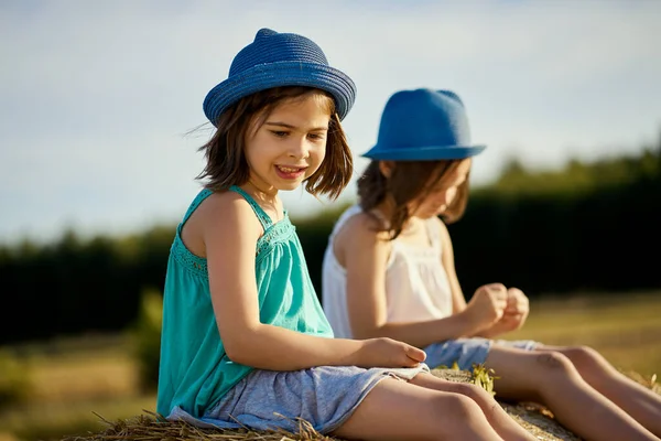 Duas meninas encantadoras estão comendo sementes de girassol no centeio cortado no campo Fotos De Bancos De Imagens Sem Royalties