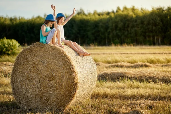 Due ragazze affascinanti sono sedute su un rotolo di segale falciata in un campo — Foto Stock