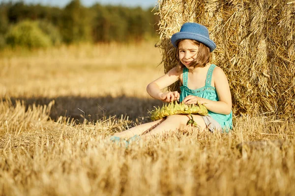 Adorable girl eating sunflower seeds on mown rye in the field — Stock Photo, Image