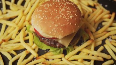 Siyah bir masada patates kızartmasıyla çevrili leziz bir çizburger.