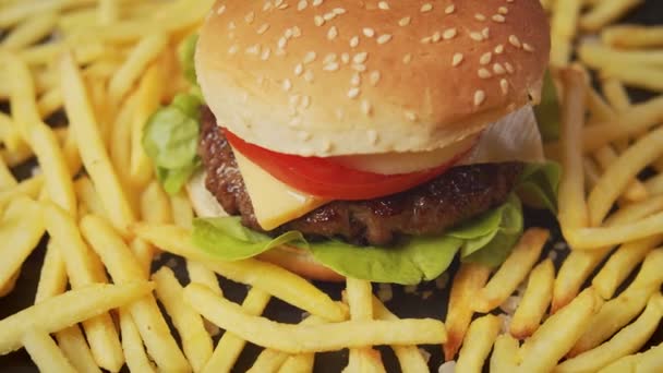 Смачний чізбургер в оточенні картоплі фрі на чорному столі — стокове відео