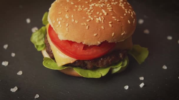 Νόστιμο cheeseburger σε ένα μαύρο τραπέζι με κρυστάλλους αλάτι — Αρχείο Βίντεο