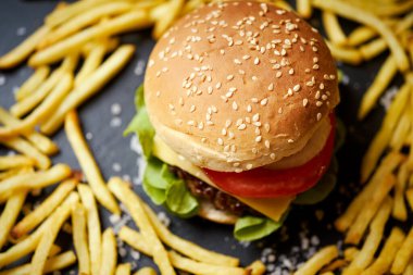 Siyah bir masada patates kızartmasıyla çevrili leziz bir çizburger.