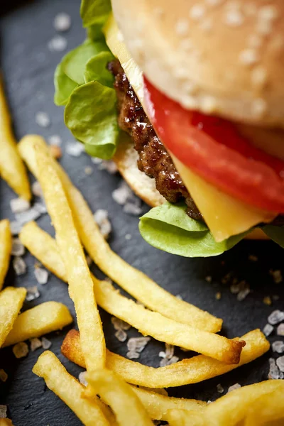 Deliciosa hamburguesa con queso rodeada de papas fritas en una mesa negra — Foto de Stock