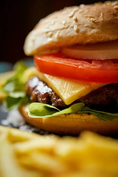 Deliciosa hamburguesa con queso rodeada de papas fritas en una mesa negra — Foto de Stock
