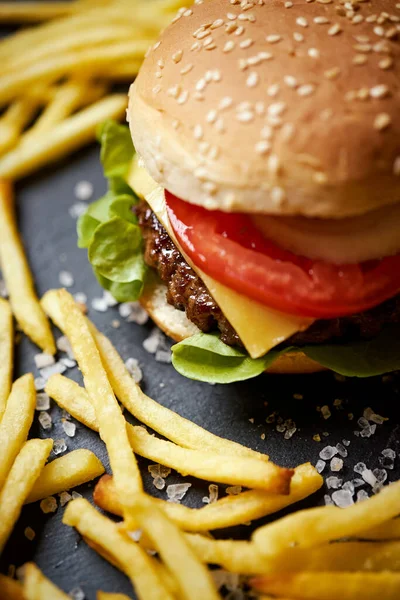 Deliciosa hamburguesa con queso rodeada de papas fritas en una mesa negra — Foto de Stock