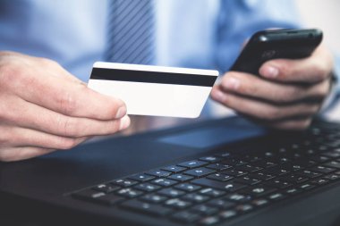 Adam kredi kartı tutuyor ve telefon kullanıyor..