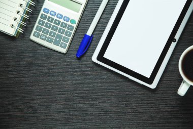 Dijital tablet, hesap makinesi, kalem, kahve ve koyu ahşap arka plan üstünde not etmek. İş kavramı