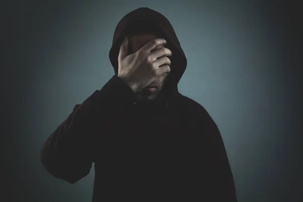Desperate hooded man covering his face on dark room.