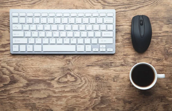 White computer keyboard, computer mouse and coffee cup on wooden desk. Business concept
