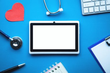 Tablet, stetoskop, kırmızı kalp, Not defteri, bilgisayar klavye mavi zemin üzerine. Tıp kavramı