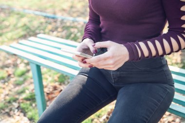 Park yerinde oturan ve telefon kullanan bir kadın..