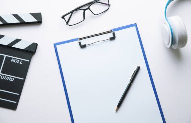 Film clapper, pano, kulaklık, gözlük ve kalem beyaz masa.