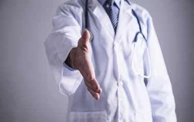 Beyaz önlük içinde tıp doktoru elini uzatıyor.