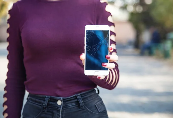 Woman holding broken smartphone in outdoor.