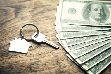 House key and dollars on a wood background.