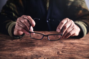 Ahşap masa gözlük tutan yaşlı kadın.