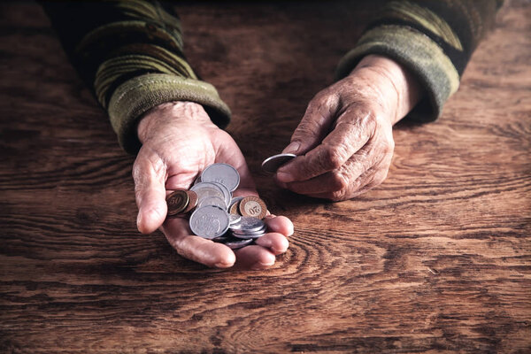 Elderly woman showing coins on wooden table.