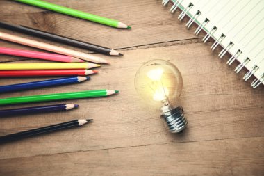 Not defteri ve kalemleri ahşap arka plan üzerinde ampul.