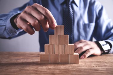 İş adamı tahta bir masanın üzerinde tahta küpü tutuyor..