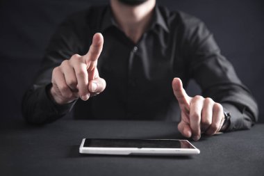 Bir tablet bilgisayar ile siyah ofis masasında adam.