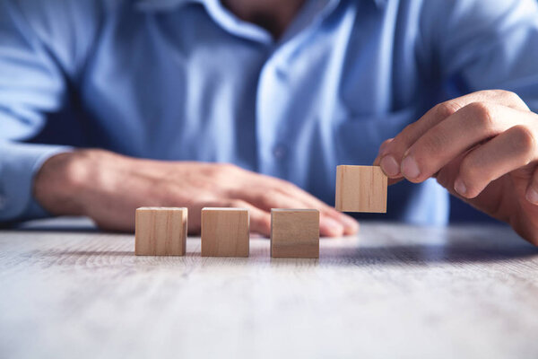 Businessman holding wooden cube on a wooden table.