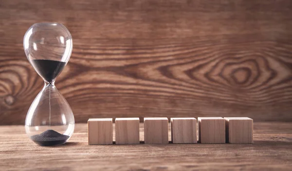 Zandloper met houten blokjes op houten ondergrond. — Stockfoto