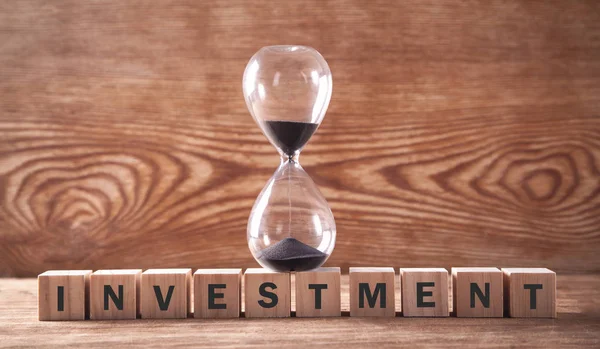 Investitionstext auf Holzwürfeln mit Sanduhr. Zeit zu investieren — Stockfoto