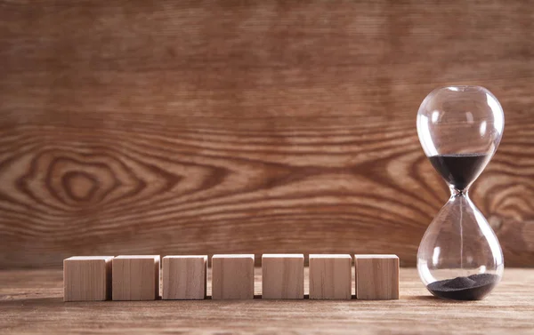 Zandloper met houten blokjes op houten ondergrond. — Stockfoto