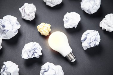 Siyah arka planda ampul ve buruşmuş kağıtlar. Fikir.